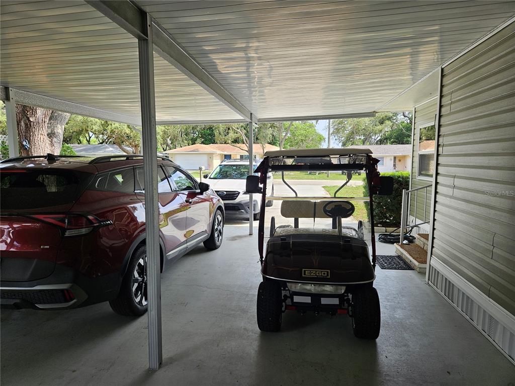 A covered carport features a parked SUV, a golf cart, and light-colored siding — 217 LAKE TARPON DRIVE UNIT 24, PALM HARBOR, FL