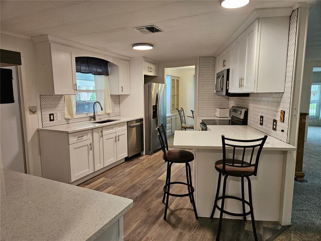 A kitchen with white cabinets, stainless steel appliances, a breakfast bar, and herringbone tile backsplash — 217 LAKE TARPON DRIVE UNIT 24, PALM HARBOR, FL