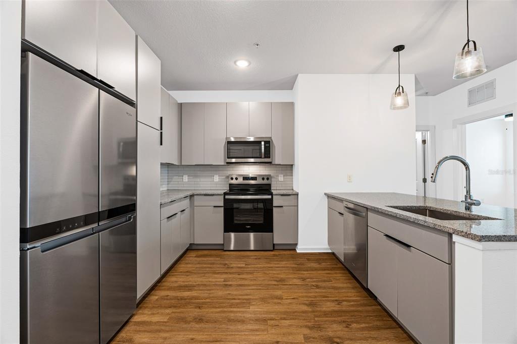 A modern kitchen features stainless steel appliances, grey cabinetry, and a granite-topped island — 1700 RANCH ROAD UNIT B1-10312, NOKOMIS, FL