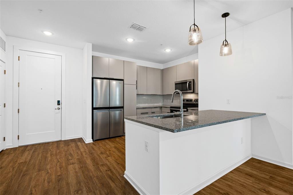 A modern kitchen features stainless steel appliances, gray cabinetry, granite countertops, and wood-look flooring — 1700 RANCH ROAD UNIT B1-10312, NOKOMIS, FL