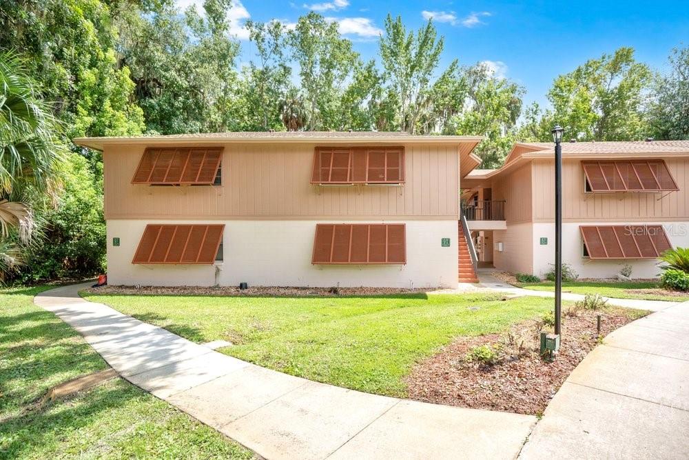 A two-story apartment building with tan siding, brown shutters, and a concrete walkway — 150 WAX MYRTLE WOODS COURT UNIT 9B, DELTONA, FL