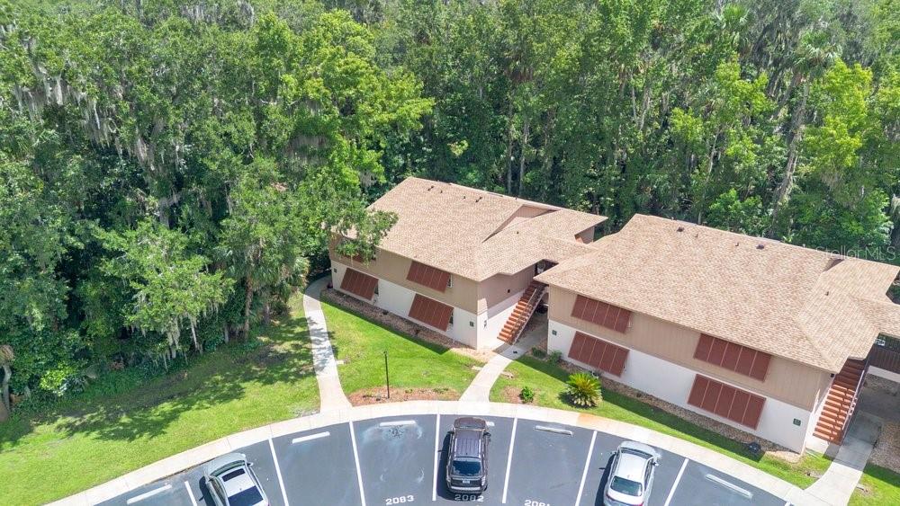 An aerial view shows a two-story apartment building with brown shutters and a parking lot — 150 WAX MYRTLE WOODS COURT UNIT 9B, DELTONA, FL