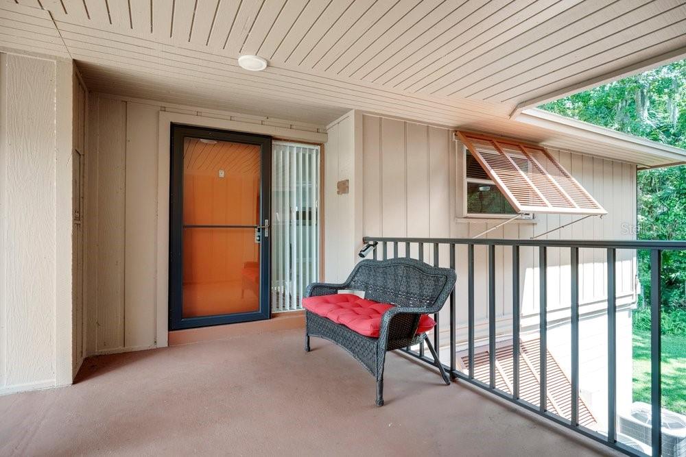 A covered balcony with a black wicker bench, a screen door, and a wooden shuttered window — 150 WAX MYRTLE WOODS COURT UNIT 9B, DELTONA, FL