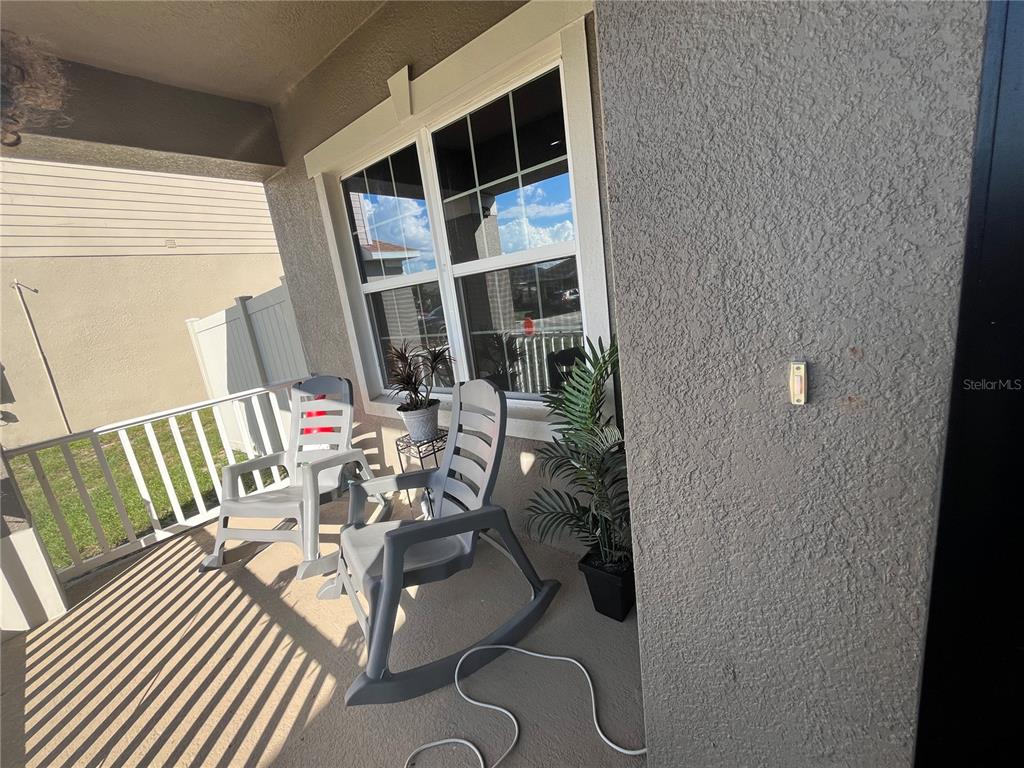 A covered porch features two gray rocking chairs, a potted plant, and a doorbell button — 823 CHINOY ROAD, DAVENPORT, FL