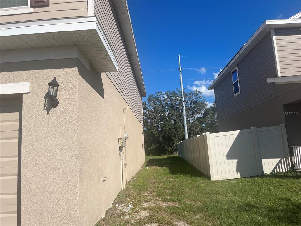 A side view of a house exterior with a grassy yard and a vinyl fence — 823 CHINOY ROAD, DAVENPORT, FL