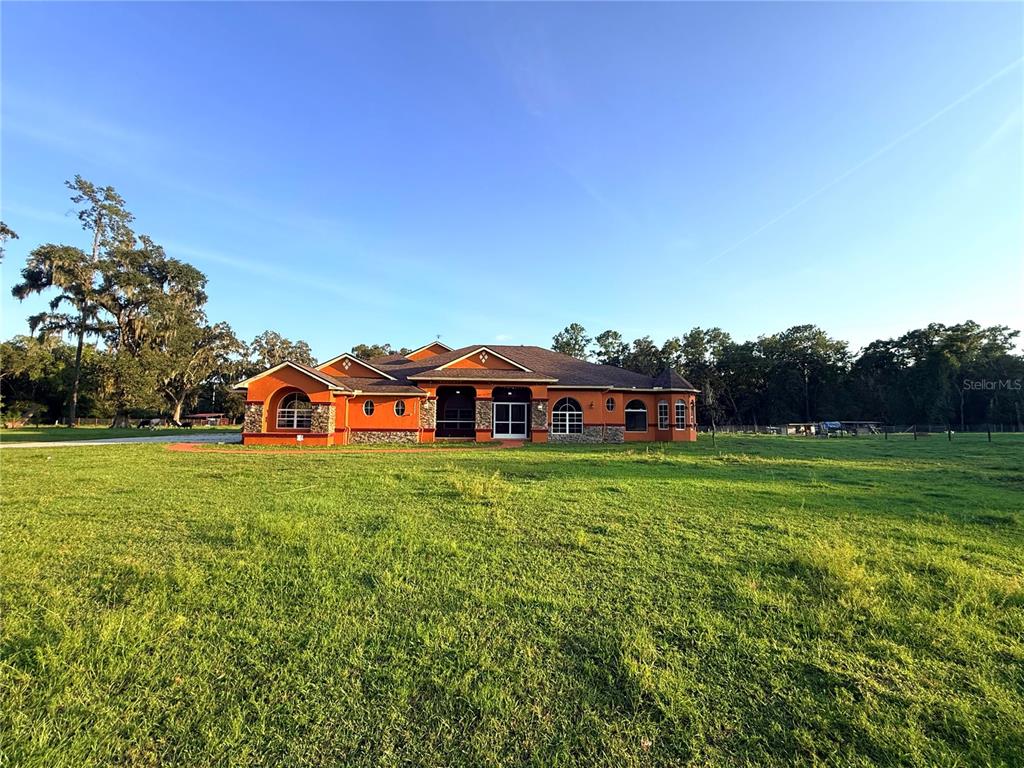A single-story orange house with stone accents sits in a large, grassy field — 25406 LADYHAWK LANE, BROOKSVILLE, FL