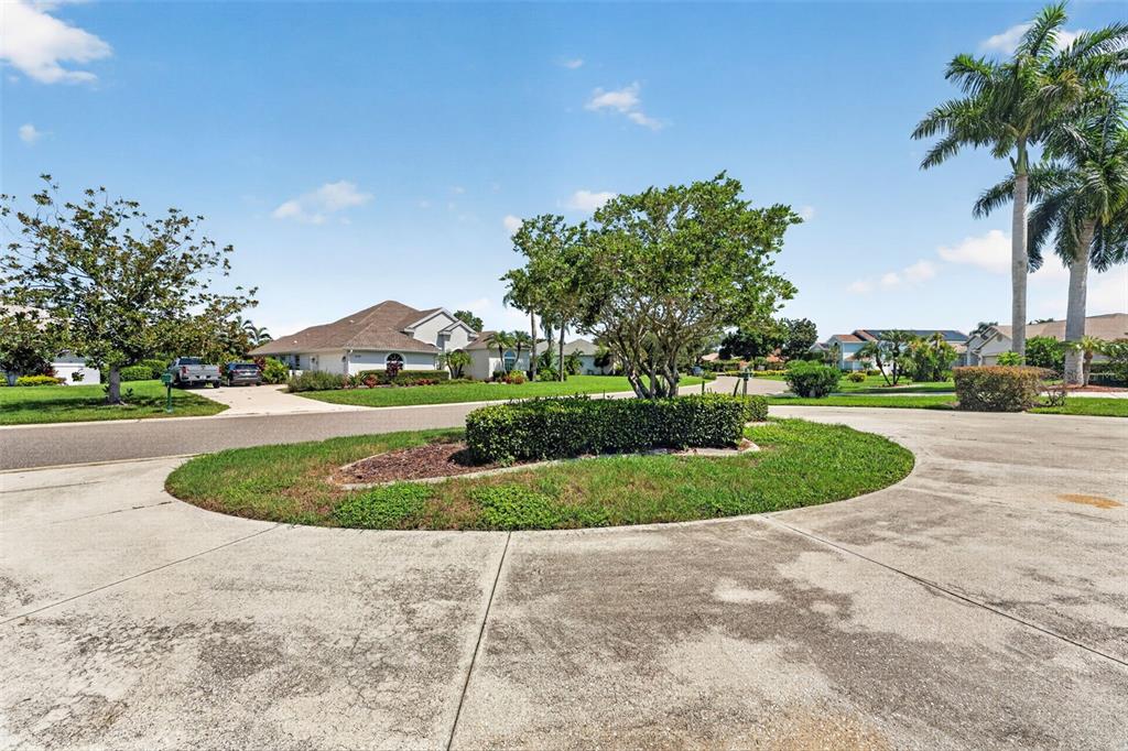 A circular driveway island with a tree and hedge sits in front of suburban houses — 2941 WILDERNESS BOULEVARD E, PARRISH, FL