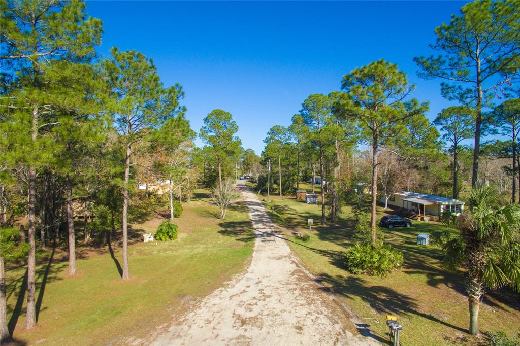 An aerial view shows a dirt road winding through a wooded residential area with mobile homes — 1211 CYPRESS ROAD, ST AUGUSTINE, FL