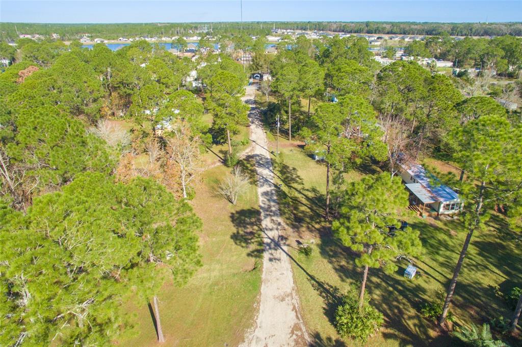 An aerial view shows a dirt driveway leading through a wooded lot toward a house — 1211 CYPRESS ROAD, ST AUGUSTINE, FL