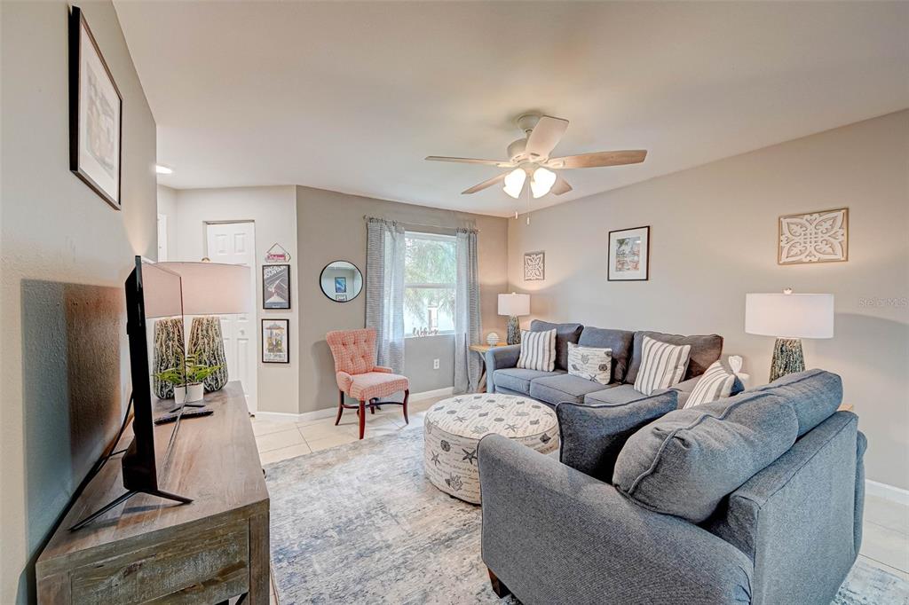A living room features a blue sofa, a patterned ottoman, and a television on a console — 3038 PARKWAY BOULEVARD UNIT 305, KISSIMMEE, FL