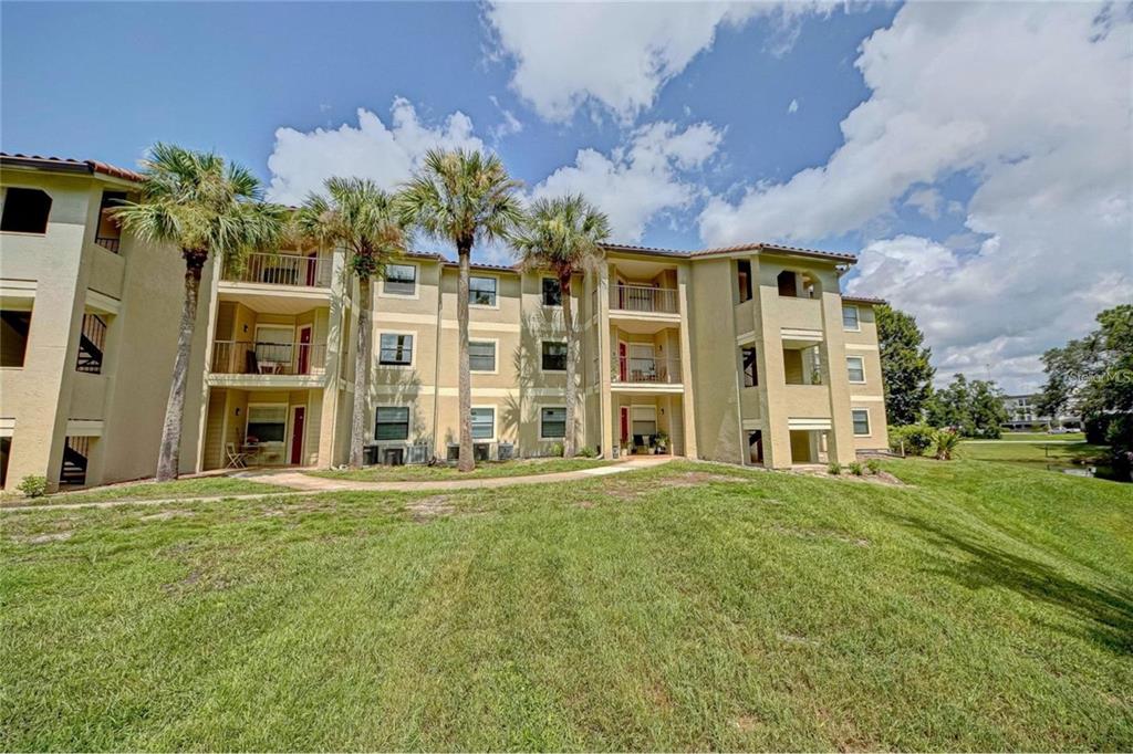 A three-story apartment building with tan stucco walls and palm trees on a grassy lawn — 3038 PARKWAY BOULEVARD UNIT 305, KISSIMMEE, FL