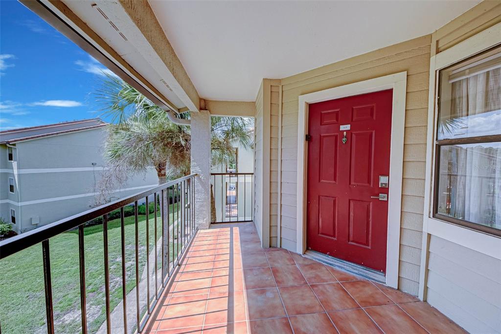 An outdoor balcony with tiled flooring, a red front door, and a metal railing — 3038 PARKWAY BOULEVARD UNIT 305, KISSIMMEE, FL