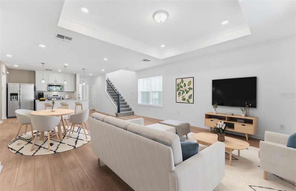 An open-concept living room and kitchen area features light wood flooring and a tray ceiling — 5322 SPRING MAIDEN CIRCLE, APOLLO BEACH, FL