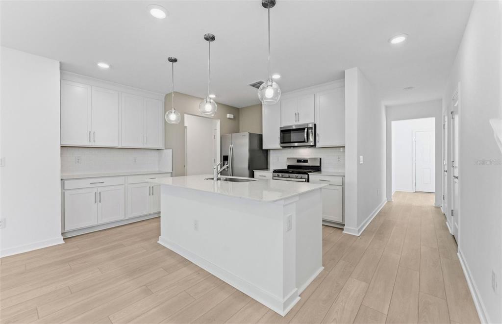 A modern kitchen features white cabinetry, a central island, stainless steel appliances, and light flooring — 5322 SPRING MAIDEN CIRCLE, APOLLO BEACH, FL
