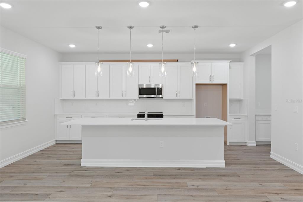 A modern kitchen features white cabinetry, a large central island, and light wood-look flooring — 6162 W CONESTOGA STREET, BEVERLY HILLS, FL