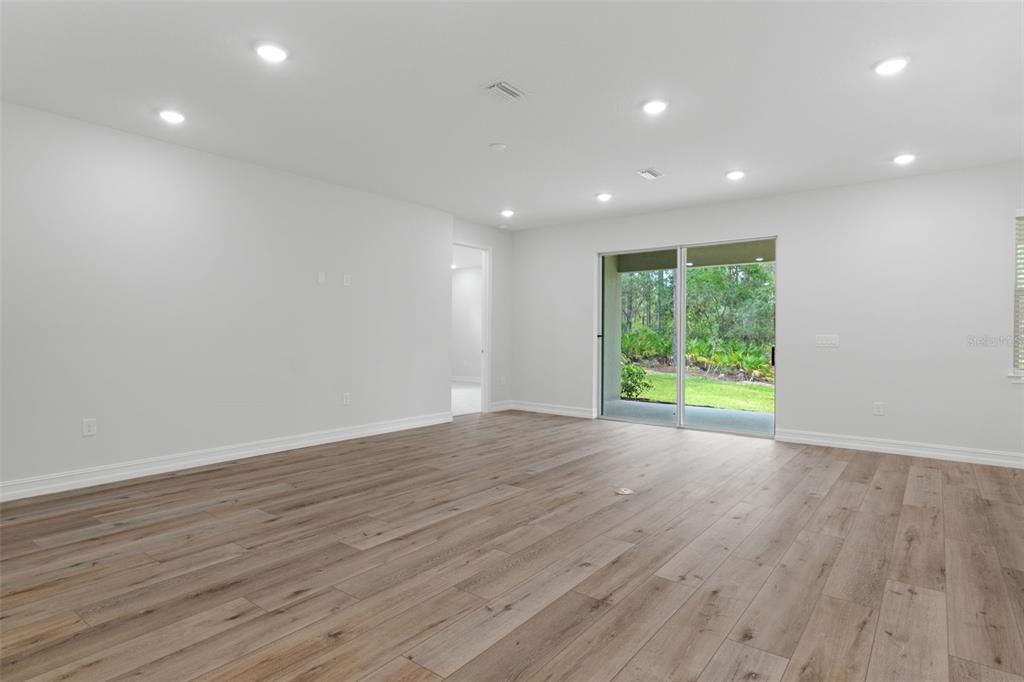 An empty living room features light wood-look flooring, white walls, recessed lighting, and sliding glass doors — 6162 W CONESTOGA STREET, BEVERLY HILLS, FL