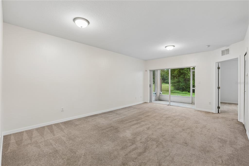 An empty carpeted room features white walls, two ceiling lights, and sliding glass doors — 522 VILLA DEL SOL CIRCLE UNIT 101, ORLANDO, FL