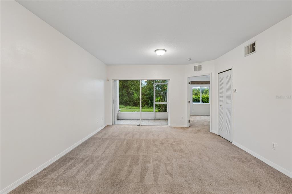 A carpeted living room with a sliding glass door leading to a screened-in patio — 522 VILLA DEL SOL CIRCLE UNIT 101, ORLANDO, FL