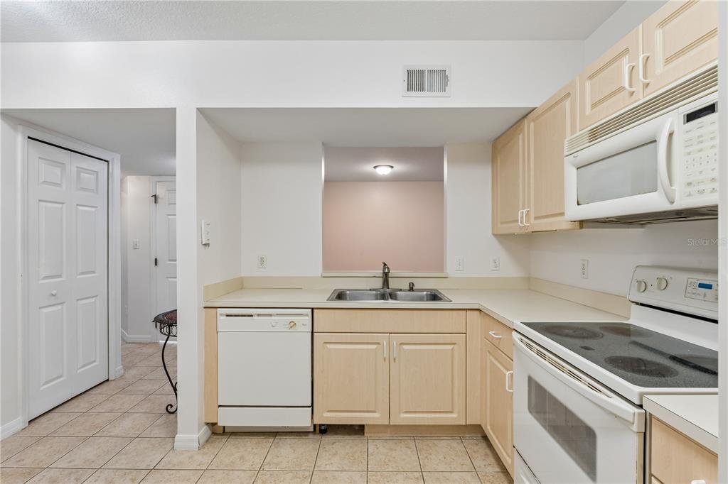 A kitchen with light wood cabinets, white appliances, a double sink, and tiled flooring — 522 VILLA DEL SOL CIRCLE UNIT 101, ORLANDO, FL