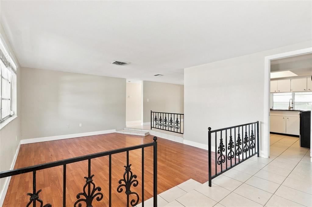 A living room features wood-look flooring, white walls, and decorative black metal railings — 5600 ANDREA DRIVE, HOLIDAY, FL