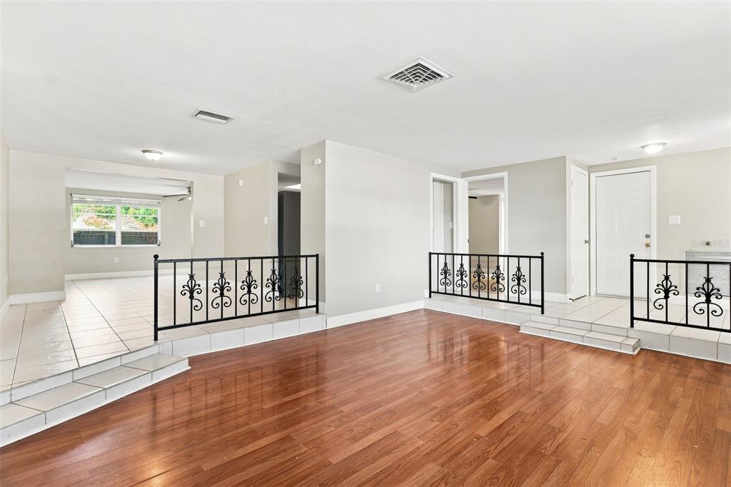 A sunken living room with wood flooring features tiled raised areas with black metal railings — 5600 ANDREA DRIVE, HOLIDAY, FL