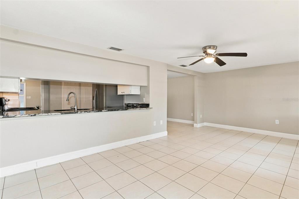 A room with light-colored tile flooring, a ceiling fan, and a kitchen pass-through window — 5600 ANDREA DRIVE, HOLIDAY, FL