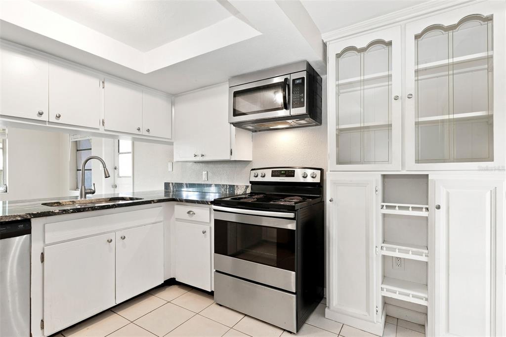 A kitchen features white cabinetry, black countertops, stainless steel appliances, and light-colored tile flooring — 5600 ANDREA DRIVE, HOLIDAY, FL