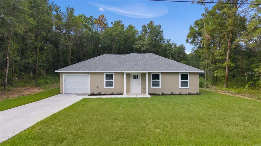A single-story house with a tan exterior, a white front door, and a concrete driveway — 14 FISHER LOOP TRACE, OCKLAWAHA, FL