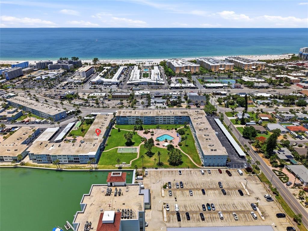 An aerial view shows a multi-story apartment complex with a pool and parking lots — 6201 2ND STREET E UNIT 106, ST PETE BEACH, FL