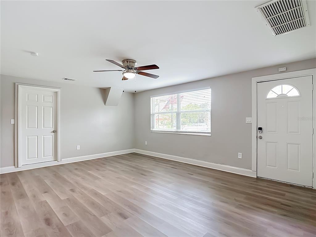 A living room with light gray walls, wood-look flooring, a ceiling fan, and an exterior door — 14402 13TH STREET, DADE CITY, FL