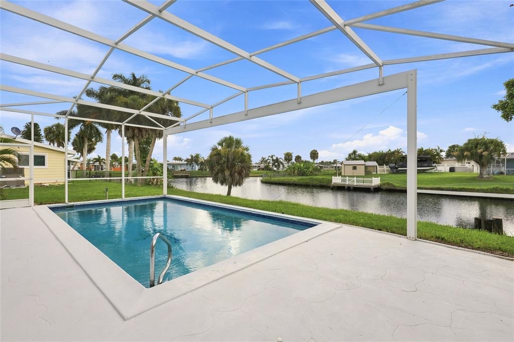 A screened-in pool patio overlooks a canal with palm trees and neighboring houses in the background — 6488 ANGLE PLACE, NORTH PORT, FL