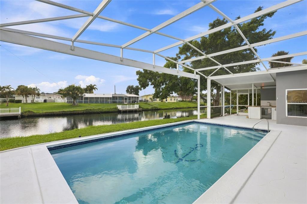 A screened-in swimming pool overlooks a canal with a dock and neighboring houses — 6488 ANGLE PLACE, NORTH PORT, FL