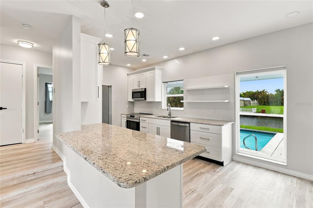 A modern kitchen features white cabinetry, granite countertops, stainless steel appliances, and a pool view — 6488 ANGLE PLACE, NORTH PORT, FL