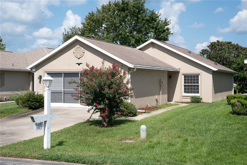 A tan, single-story house with a garage, a front lawn, and a decorative circular vent — 1913 NW 50TH CIRCLE, OCALA, FL