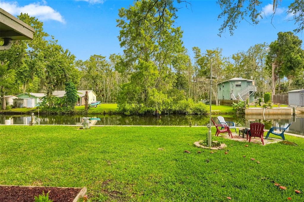 A grassy backyard overlooks a canal with trees and houses in the background — 5421 GAY STREET, WEEKI WACHEE, FL