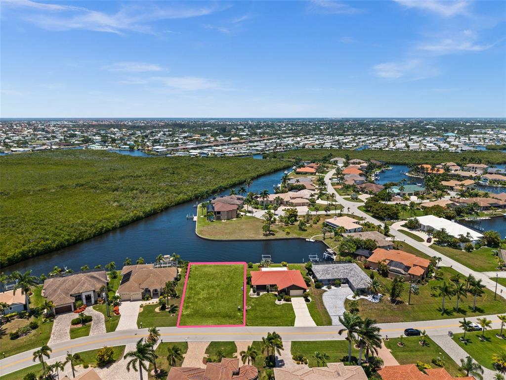 An aerial view shows a vacant waterfront lot highlighted in pink between two residential houses — 3324 TRIPOLI BOULEVARD, PUNTA GORDA, FL