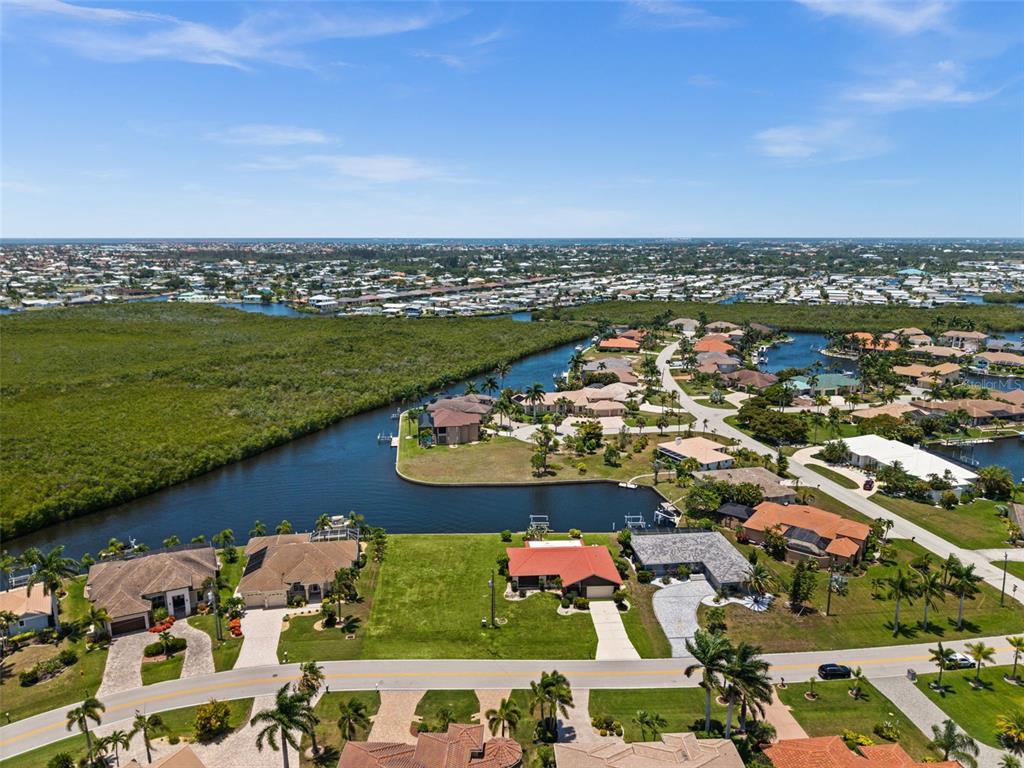 An aerial view shows waterfront homes, a canal, and dense mangroves under a blue sky — 3324 TRIPOLI BOULEVARD, PUNTA GORDA, FL