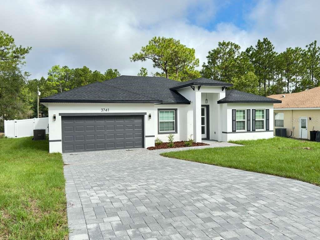 A single-story house with a white exterior, dark roof, and a gray paver driveway — 3741 W FOREST DRIVE W, DUNNELLON, FL