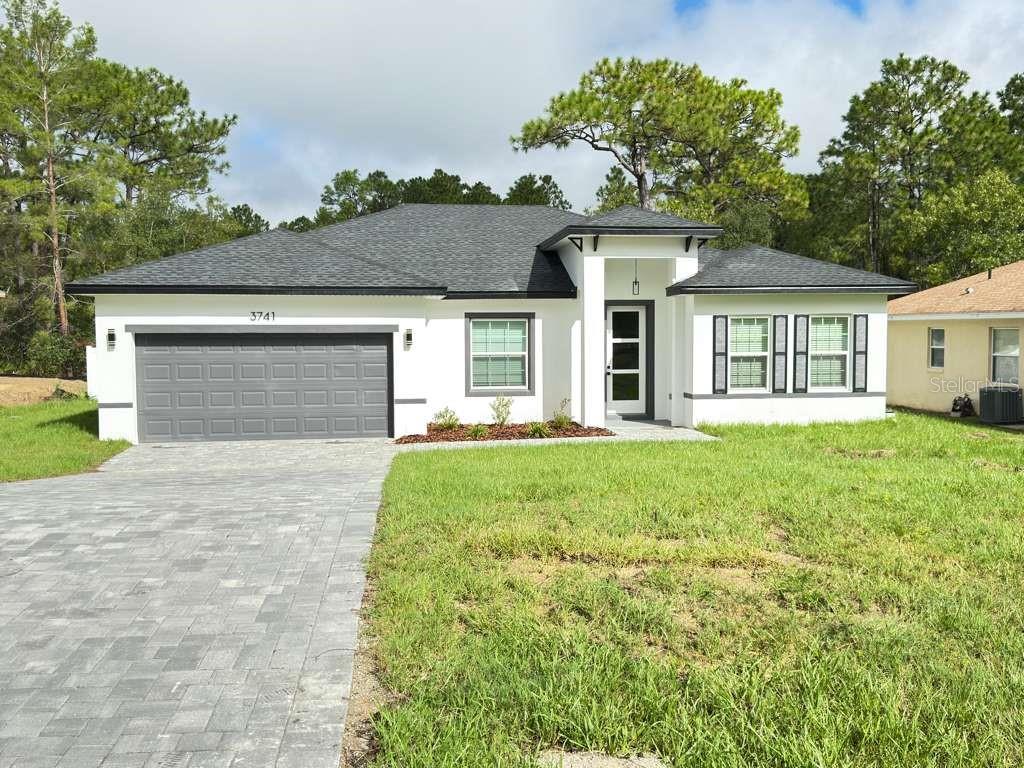 A single-story house with a white exterior, gray garage door, and a paved driveway — 3741 W FOREST DRIVE W, DUNNELLON, FL