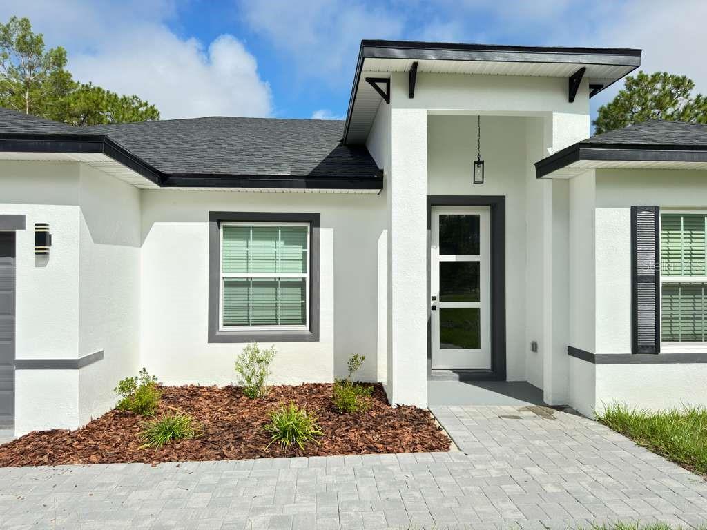 The exterior of a modern white house features a dark roof, gray trim, and pavers — 3741 W FOREST DRIVE W, DUNNELLON, FL