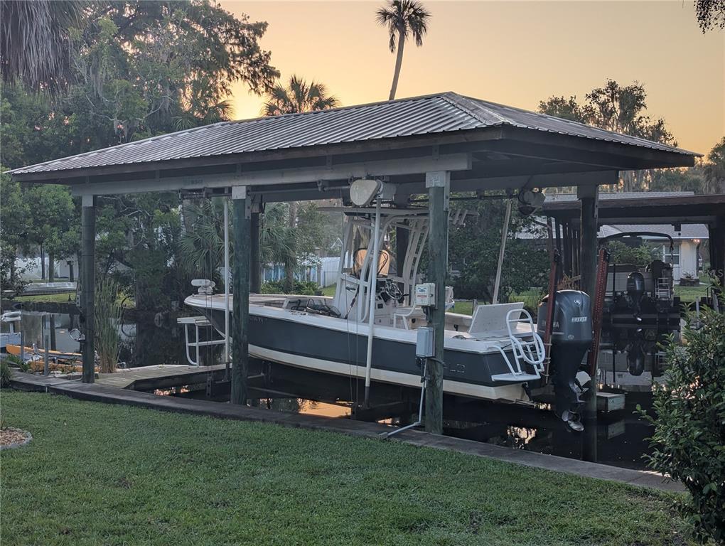 A boat sits on a lift under a covered dock structure next to a grassy lawn — 556 NW FERN DRIVE, CRYSTAL RIVER, FL