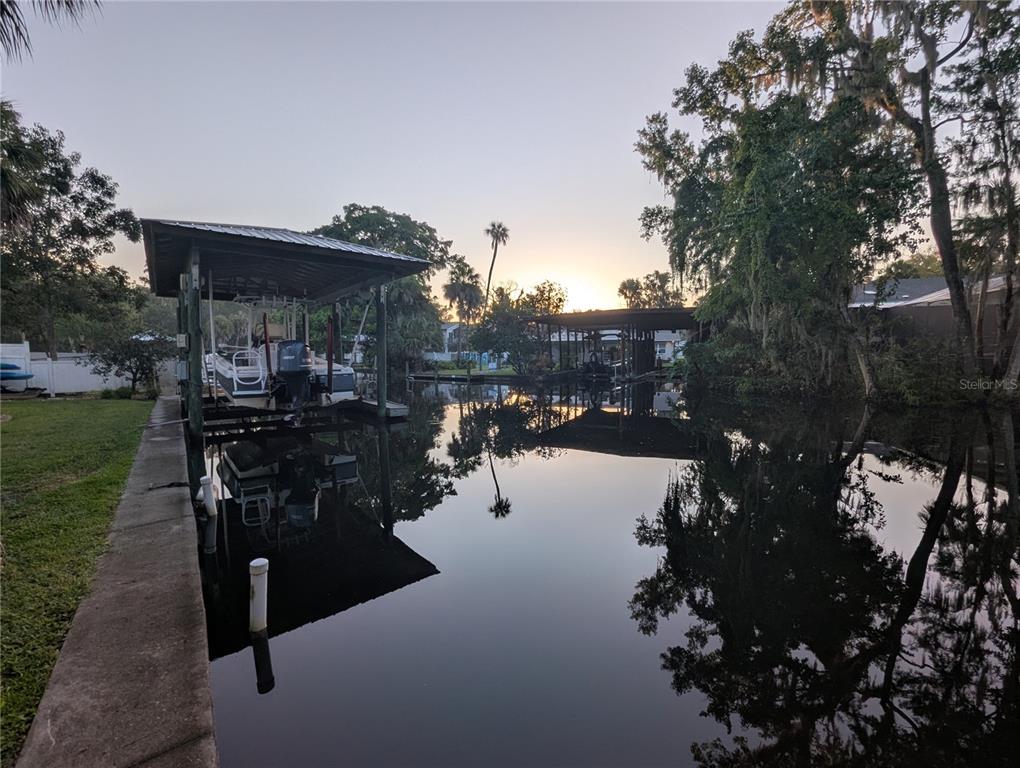 A boat lift sits on a calm canal at sunset with trees reflecting in the water — 556 NW FERN DRIVE, CRYSTAL RIVER, FL