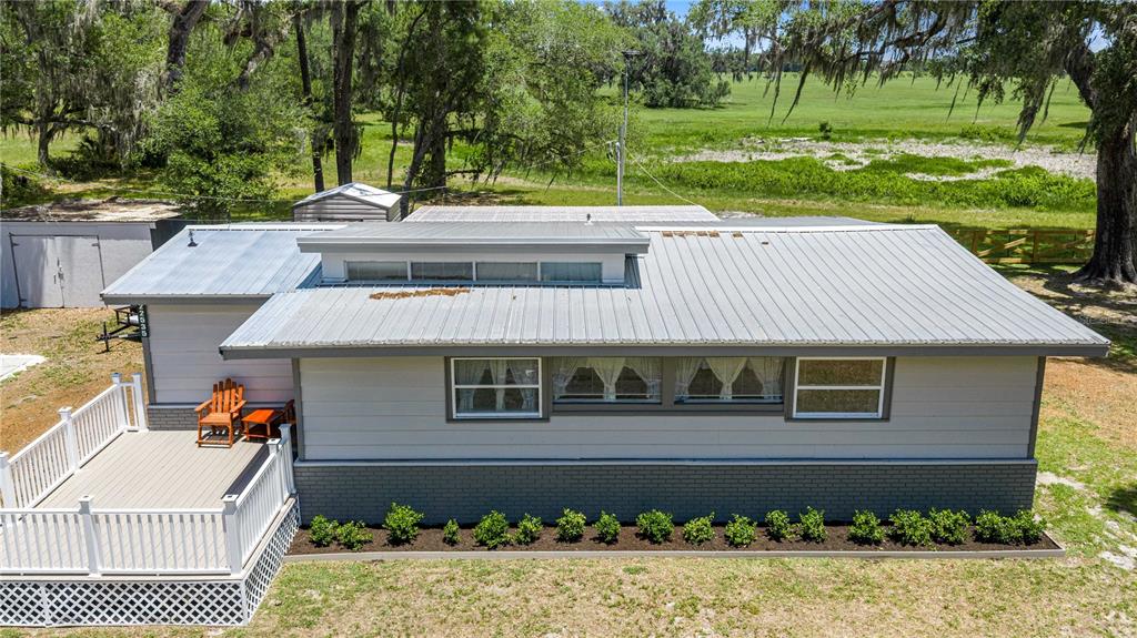 A light-colored house exterior features a wooden deck, white railings, and two wooden chairs — 22535 SW 117TH STREET, DUNNELLON, FL