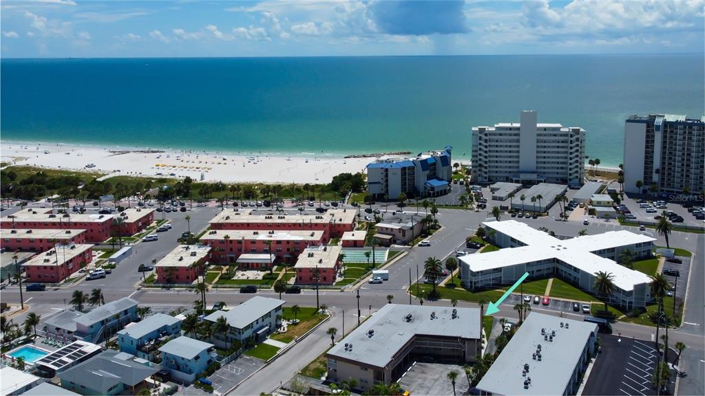 An aerial view shows a coastal neighborhood with multi-story apartment buildings near a sandy beach — 7003 SUNSET WAY UNIT 1, ST PETE BEACH, FL