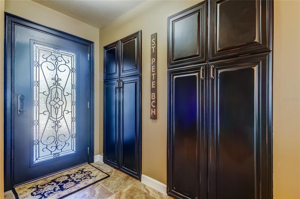 An entryway features a dark blue door with decorative glass, dark cabinetry, and tiled flooring — 7003 SUNSET WAY UNIT 1, ST PETE BEACH, FL