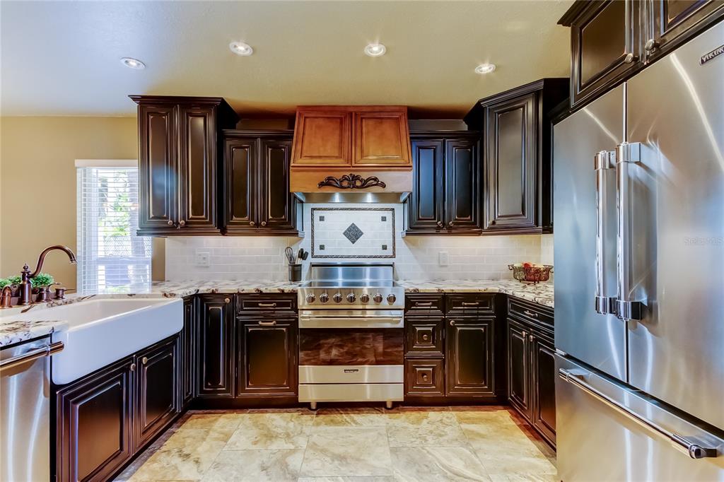 A kitchen features dark wood cabinets, stainless steel appliances, a farmhouse sink, and stone countertops — 7003 SUNSET WAY UNIT 1, ST PETE BEACH, FL