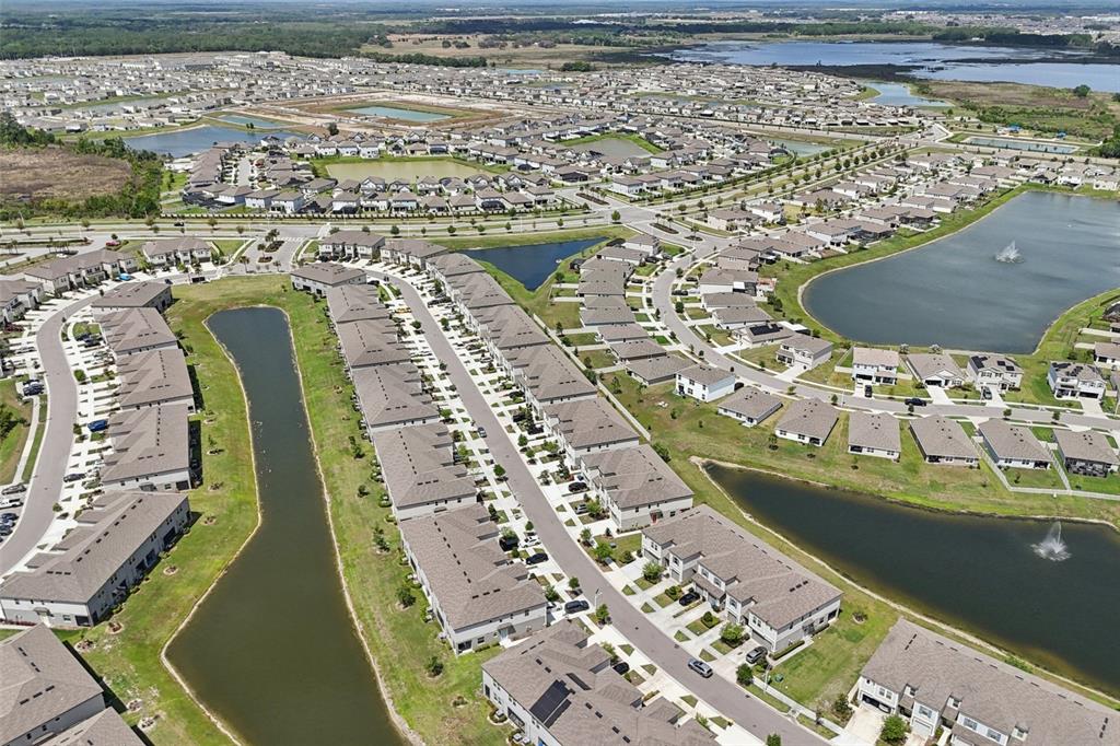 Aerial view of a suburban neighborhood featuring rows of townhomes, ponds, and paved streets — 32010 BLUE PASSING LOOP, WESLEY CHAPEL, FL