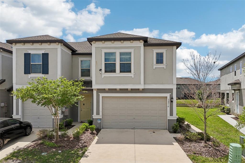 A two-story suburban house with a beige stucco exterior, a two-car garage, and a driveway — 32010 BLUE PASSING LOOP, WESLEY CHAPEL, FL