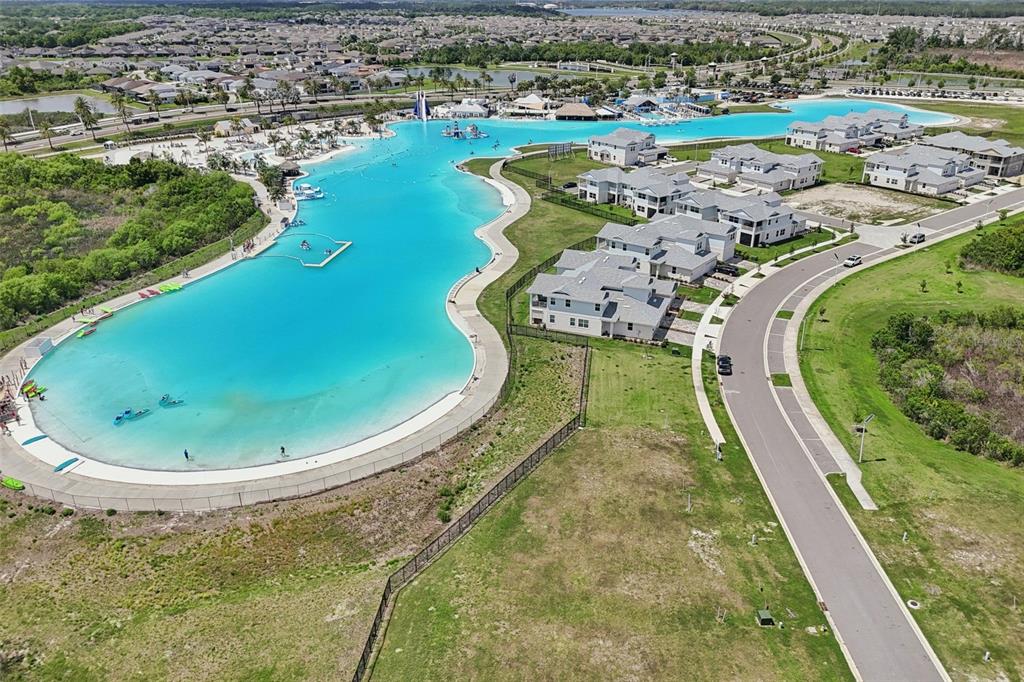 An aerial view shows a large turquoise lagoon surrounded by residential buildings and green space — 32010 BLUE PASSING LOOP, WESLEY CHAPEL, FL