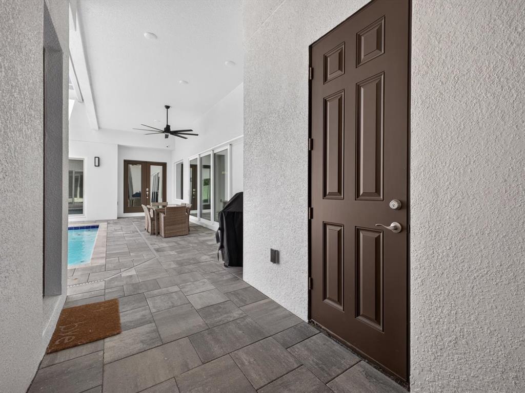 A covered patio features gray stone pavers, a swimming pool, and a brown entry door — 196 HAMPTON LOOP, DAVENPORT, FL